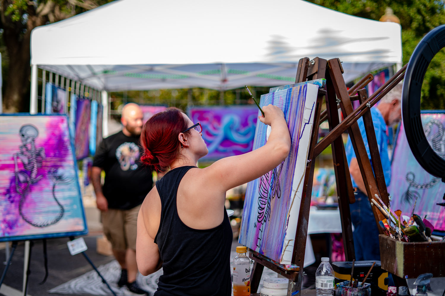Artist painting outdoors in front of an art display